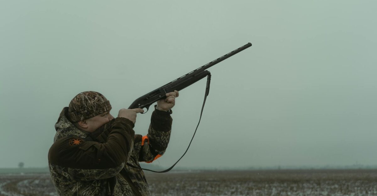 A hunter in camouflage aims a rifle in a foggy open field showcasing outdoor hunting