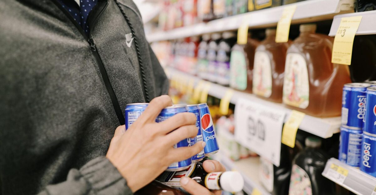 Close-up of an adult shopping for Pepsi and sauces in a grocery store aisle