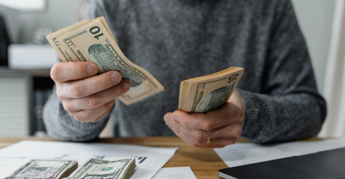 Close-up of person counting cash with a calculator and paperwork on a desk