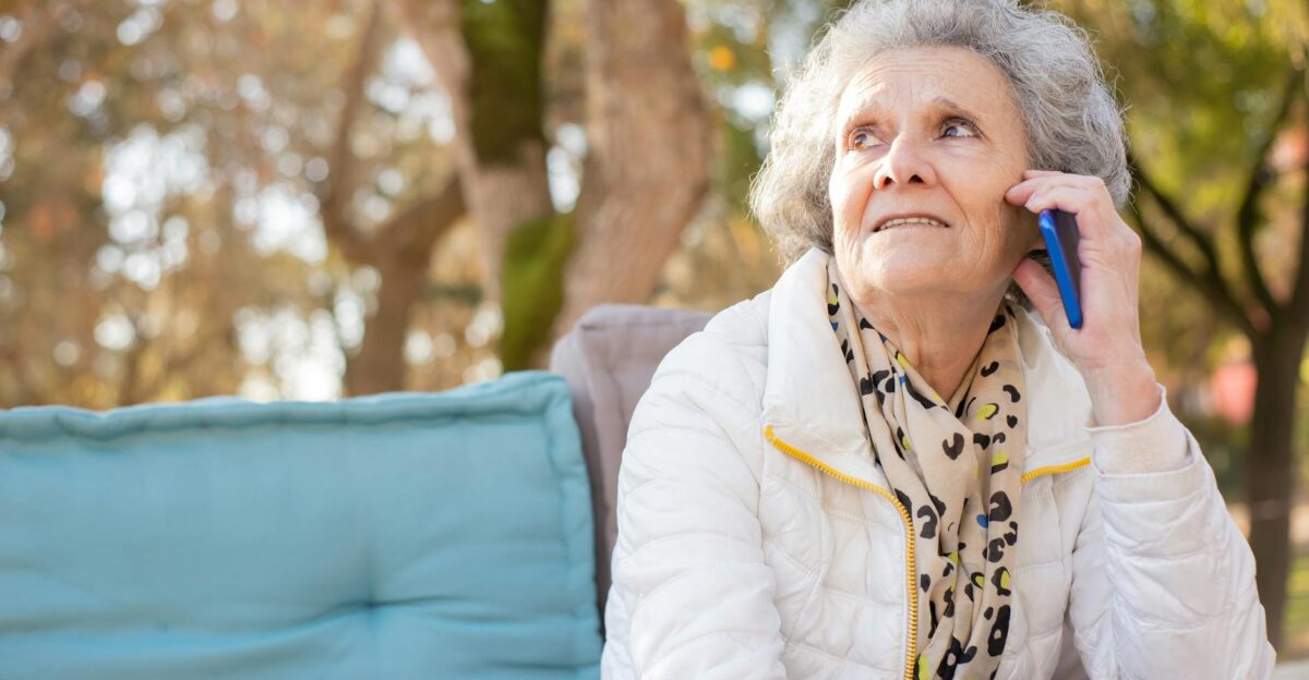 Senior woman in white jacket having a phone conversation in an outdoor park setting