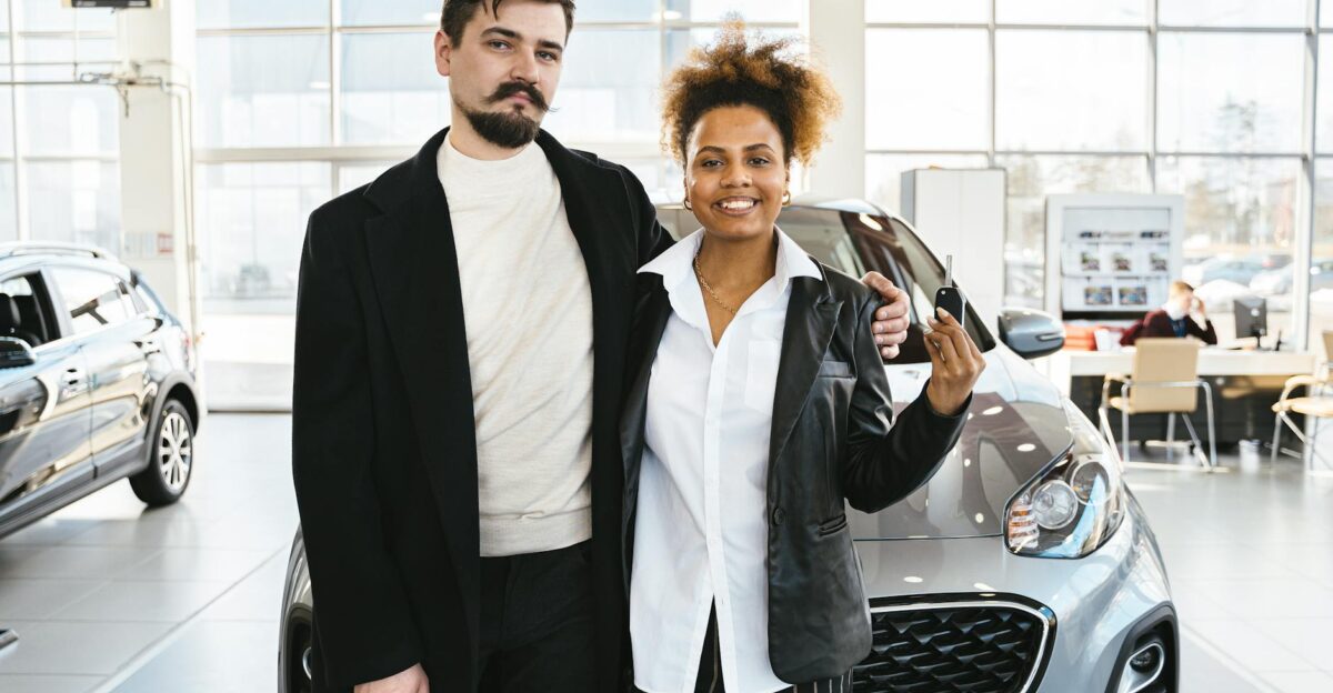 Interracial couple celebrates buying a new car at a dealership holding keys and smiling