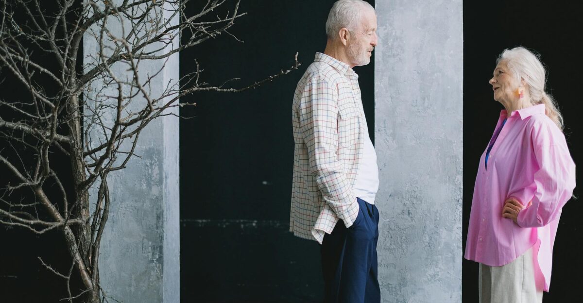 Elderly man and woman sharing a joyful conversation indoors next to a leafless tree