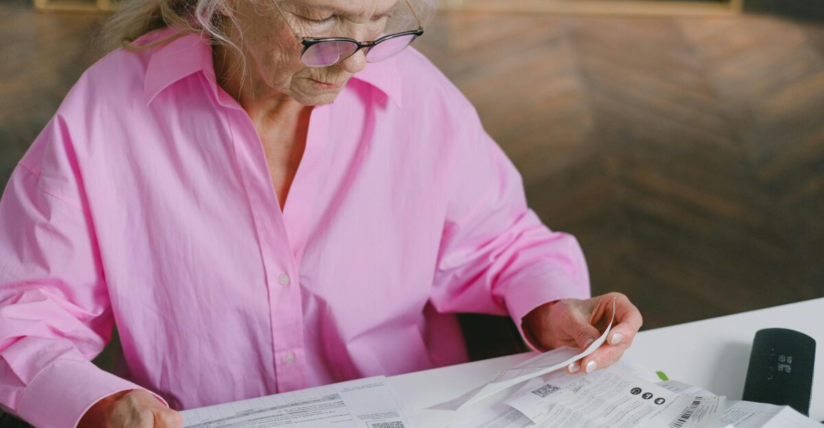 Elderly woman in pink blouse reading documents at a table indoors