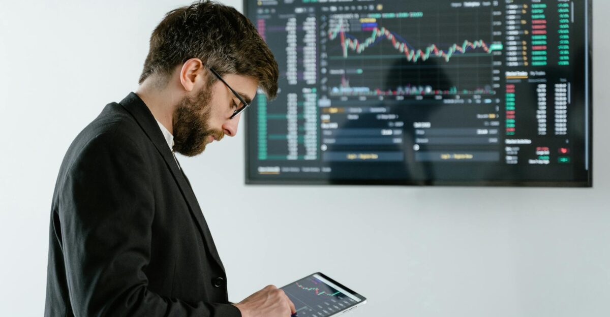 Professional man using tablet in front of cryptocurrency trading screen indoors