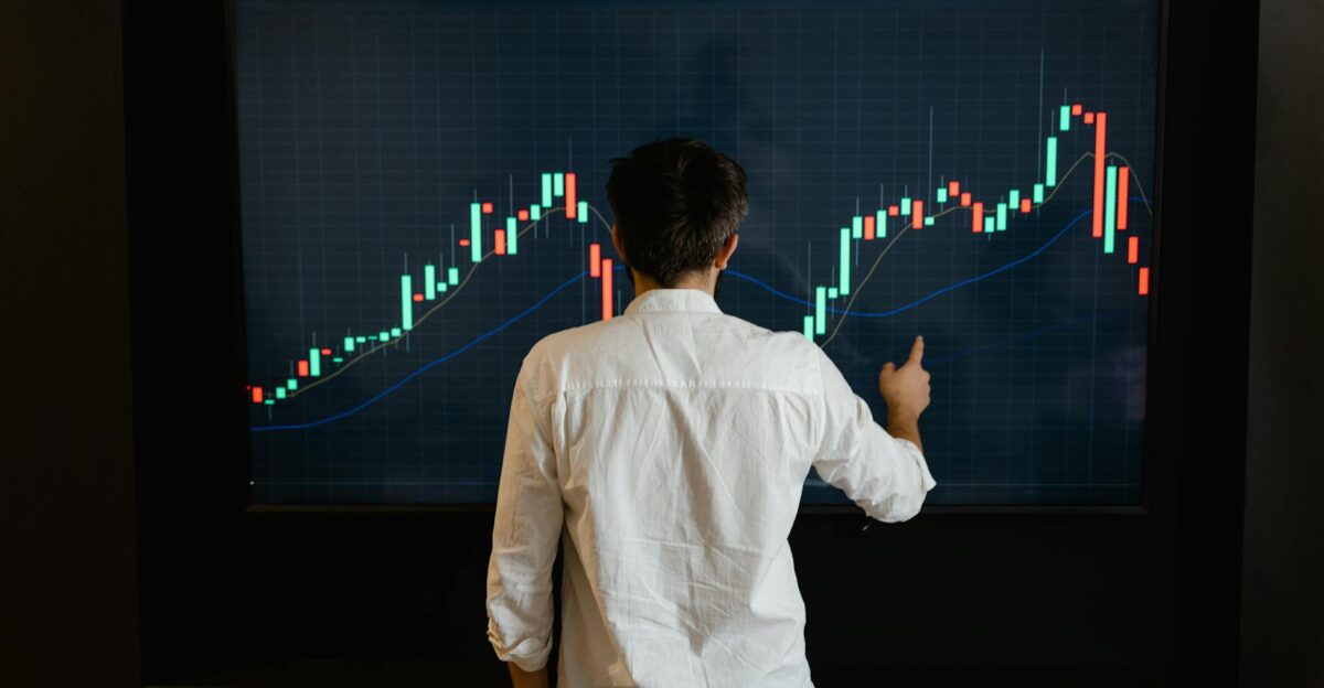 Adult male reviewing stock market data on a large display screen indoors