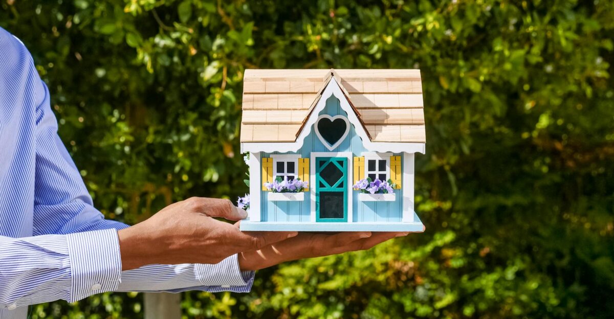 Close-up of a man s hands holding a decorative miniature house against foliage backdrop