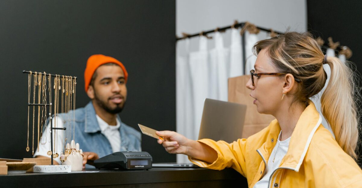 Woman in yellow jacket pays with credit card at shop counter with jewelry display