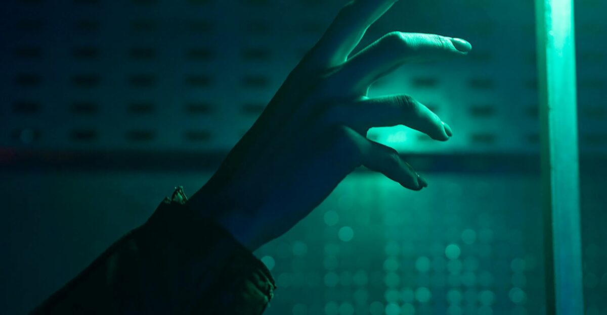 A close-up of a hand reaching out in a dimly lit environment with neon green lighting