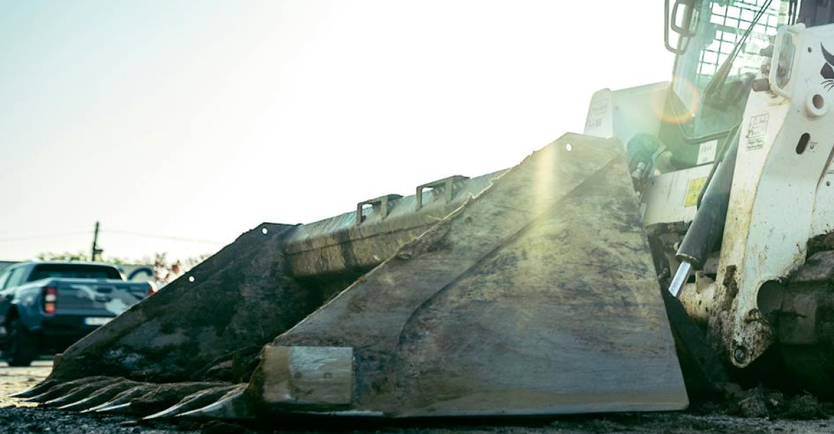 A skid steer loader on a construction site with bright sunlight in the background