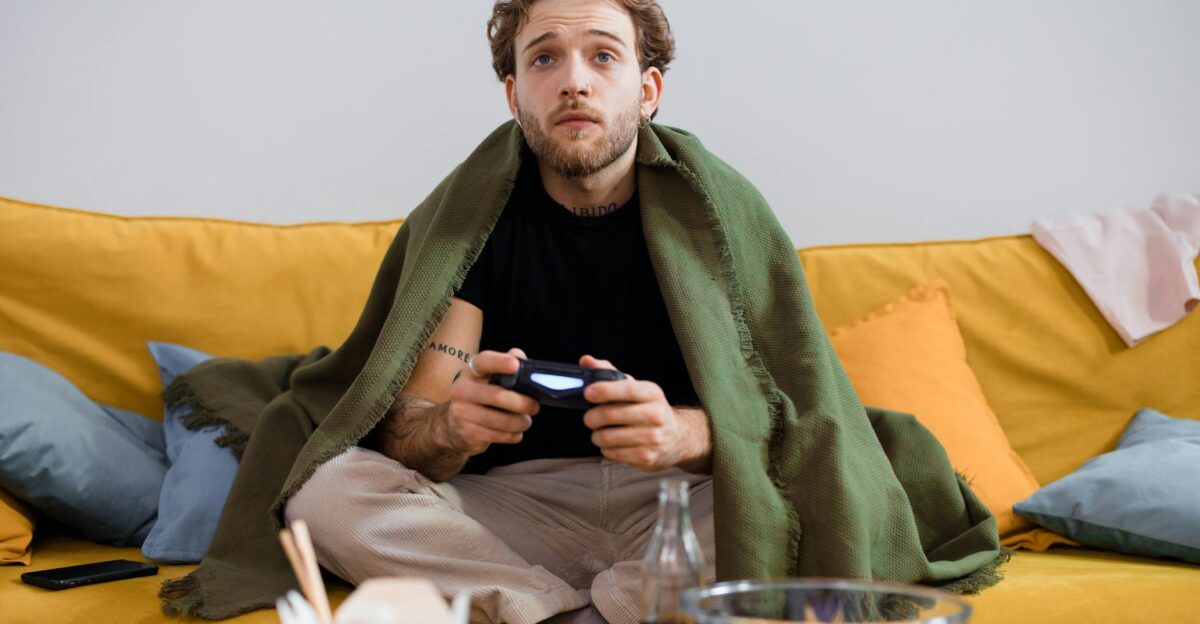 Man on couch gaming with controller wrapped in blanket offering cozy ambiance