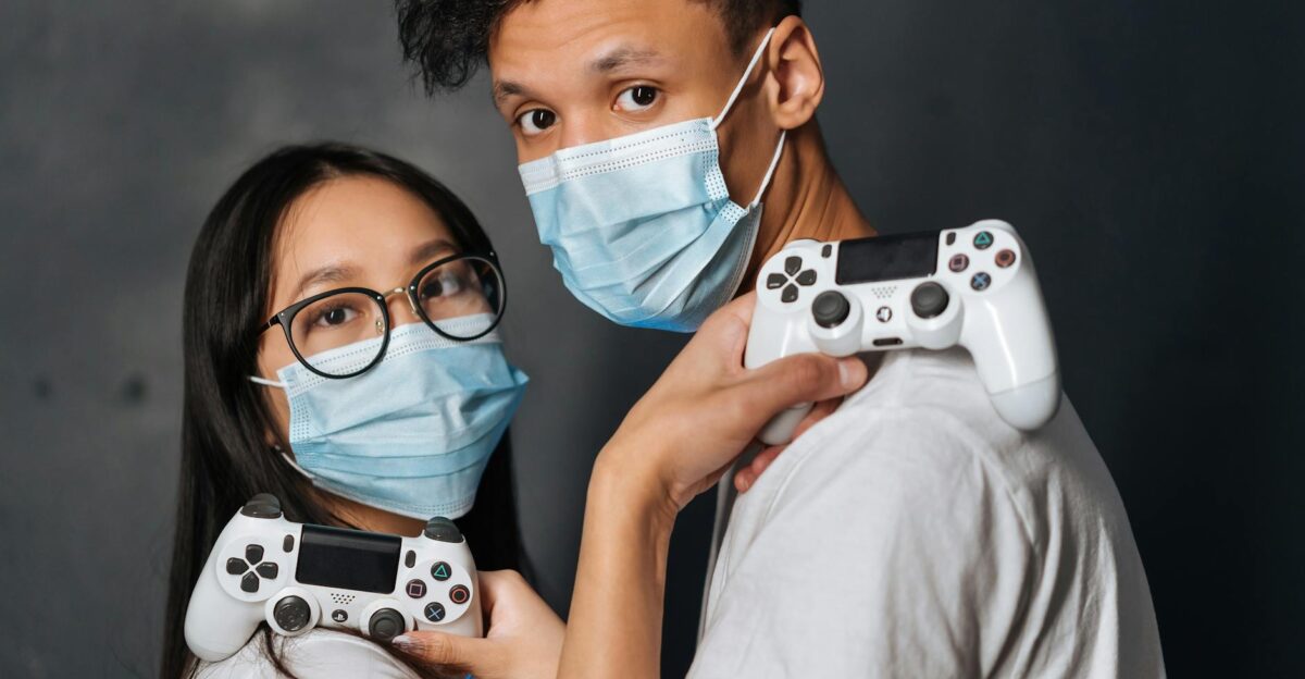 Two young adults with face masks hold game controllers capturing the modern gaming experience