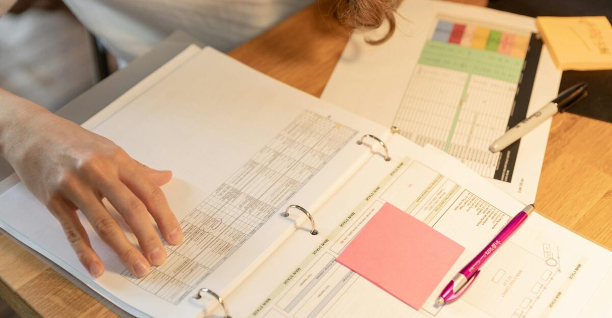 Close-up of an employee sorting documents with sticky notes and pens on a wooden desk