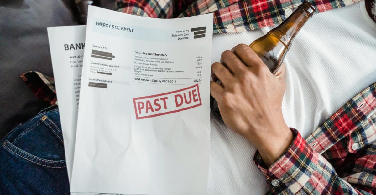 A man relaxes with a beer bottle while holding past due bills highlighting financial stress