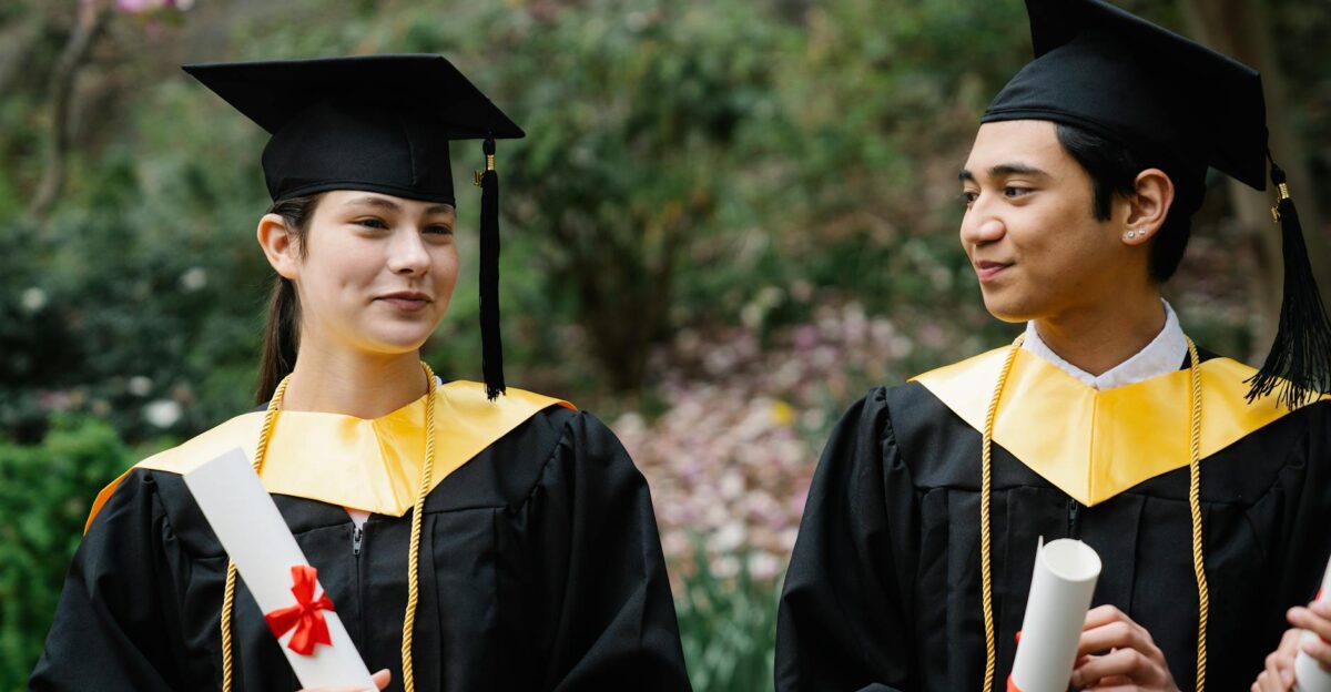 Two young graduates with diplomas celebrate their achievement in graduation caps outdoors
