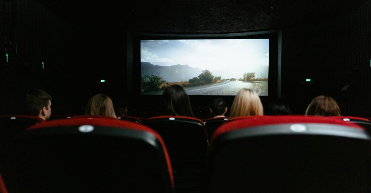 View from behind of people watching a movie in a cinema with red seats and a large screen