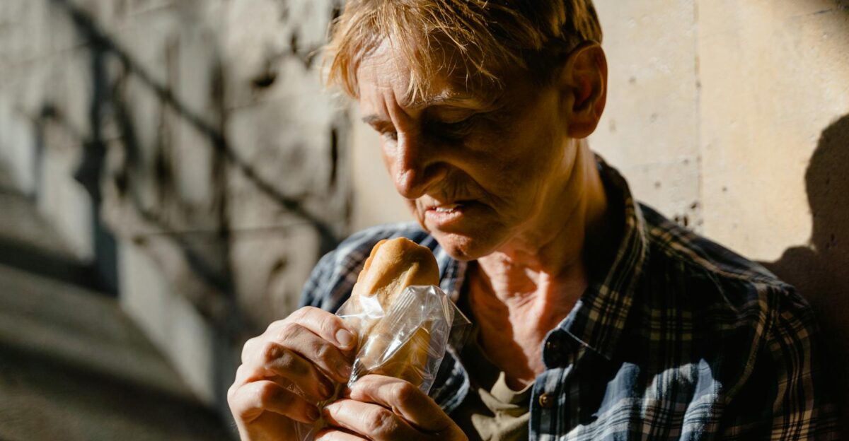 Elderly woman holding a bread roll in a sunlit shaded street corner