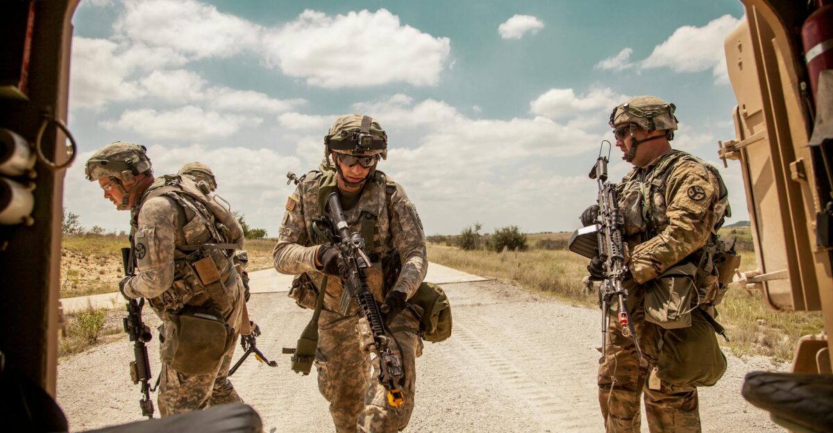 Three soldiers in camouflage gear with rifles in an outdoor military training exercise