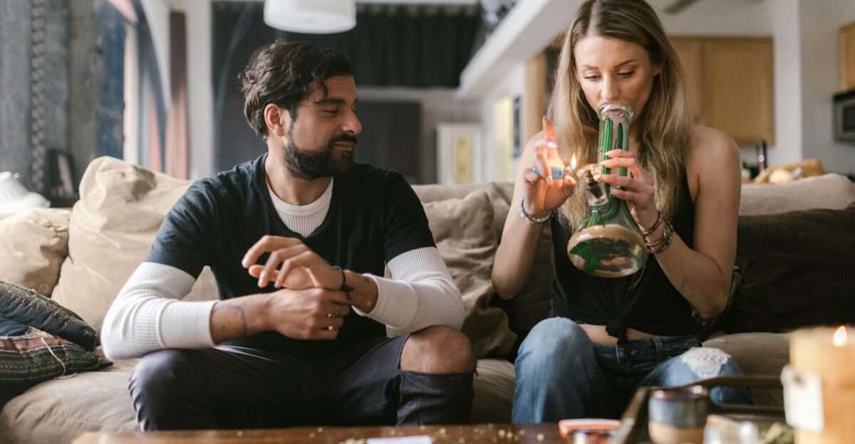 Two young adults relaxing indoors and enjoying cannabis with a bong