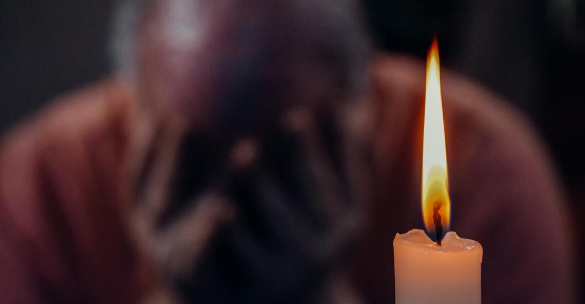 A senior adult in an emotional moment lit by a candle symbolizing reflection and grief