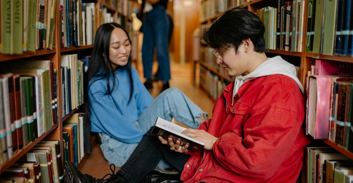 Two students sitting on a library floor reading and discussing books