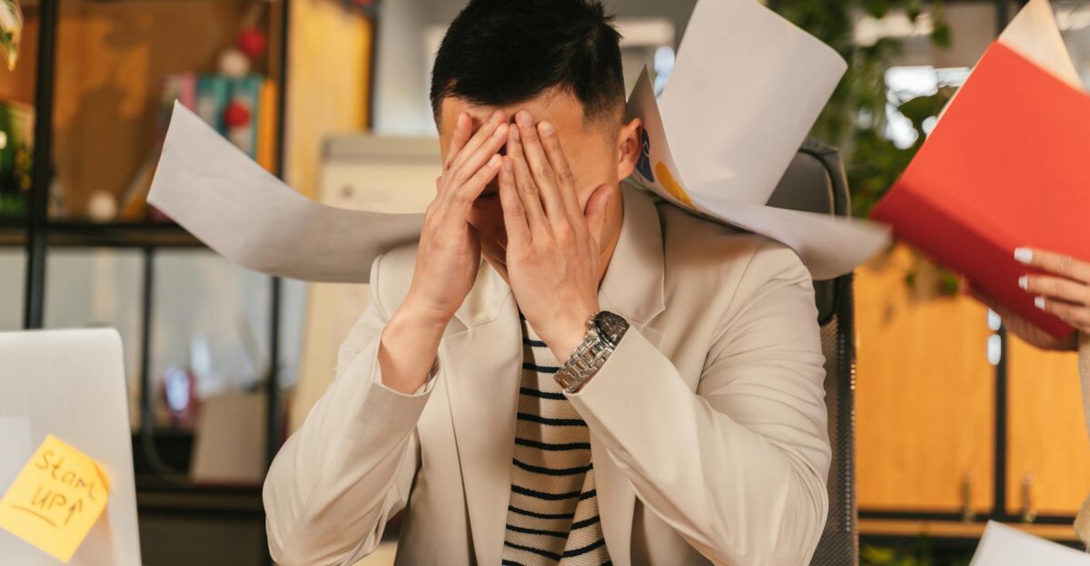 Stressed businessman overwhelmed by paperwork in office environment demonstrating burnout