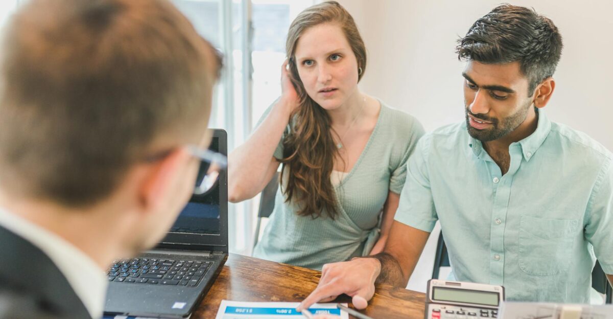 A young couple consults with a realtor about buying a home indoors in a modern office setting