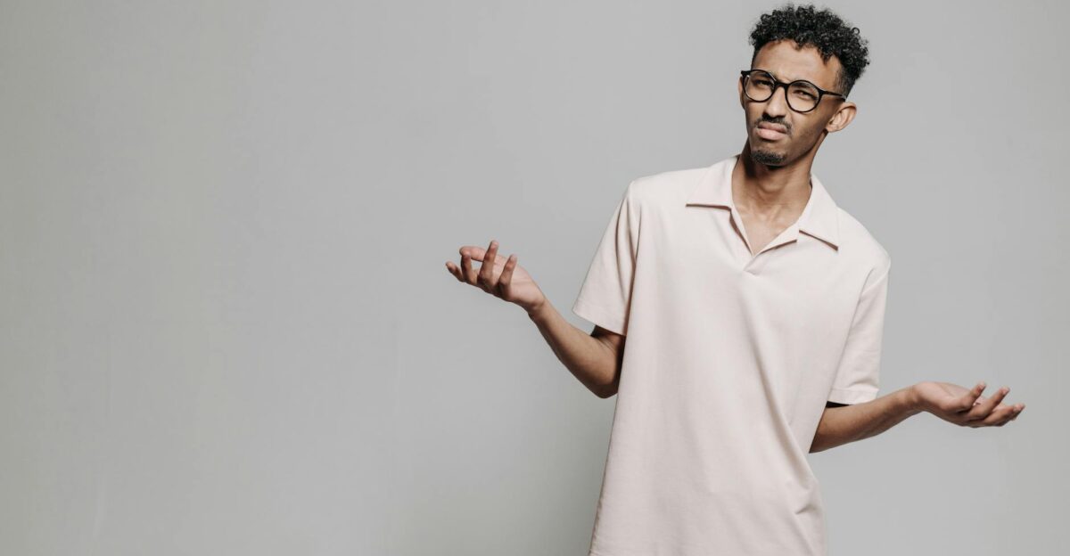 Studio portrait of a young African American man wearing eyeglasses and a white polo shirt expressing confusion