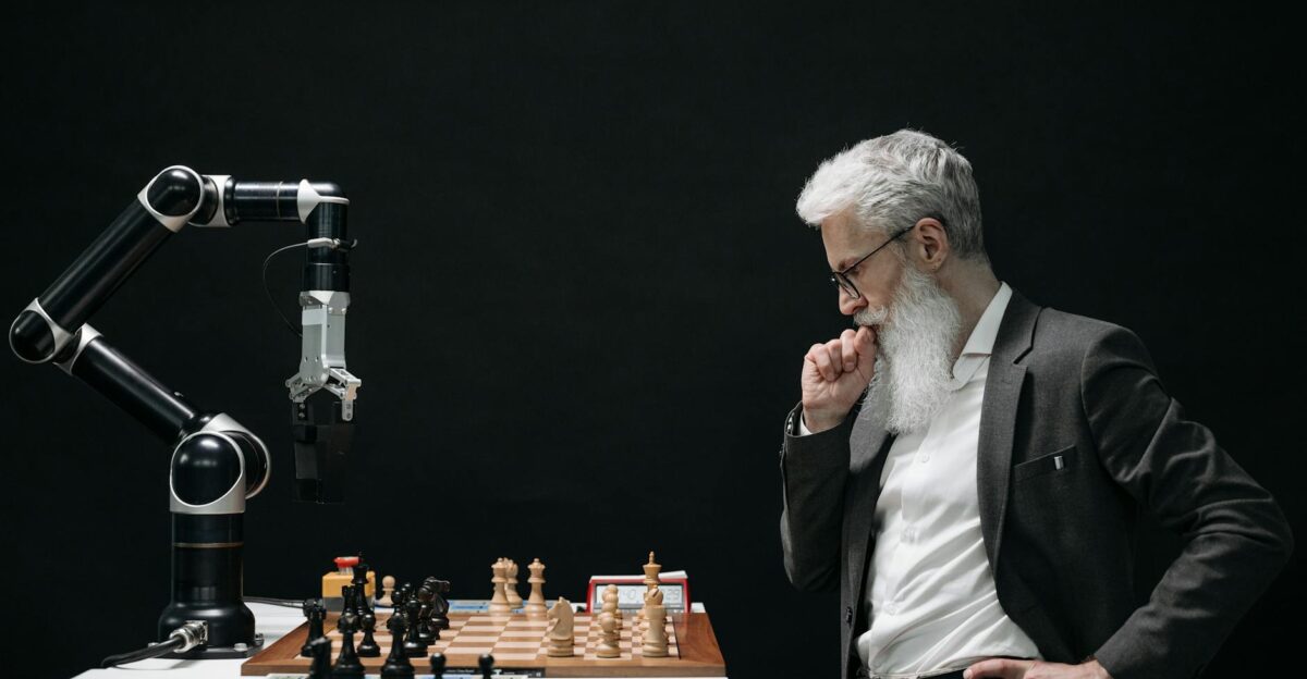 An elderly scientist contemplates a chess move against a robotic arm on a chessboard
