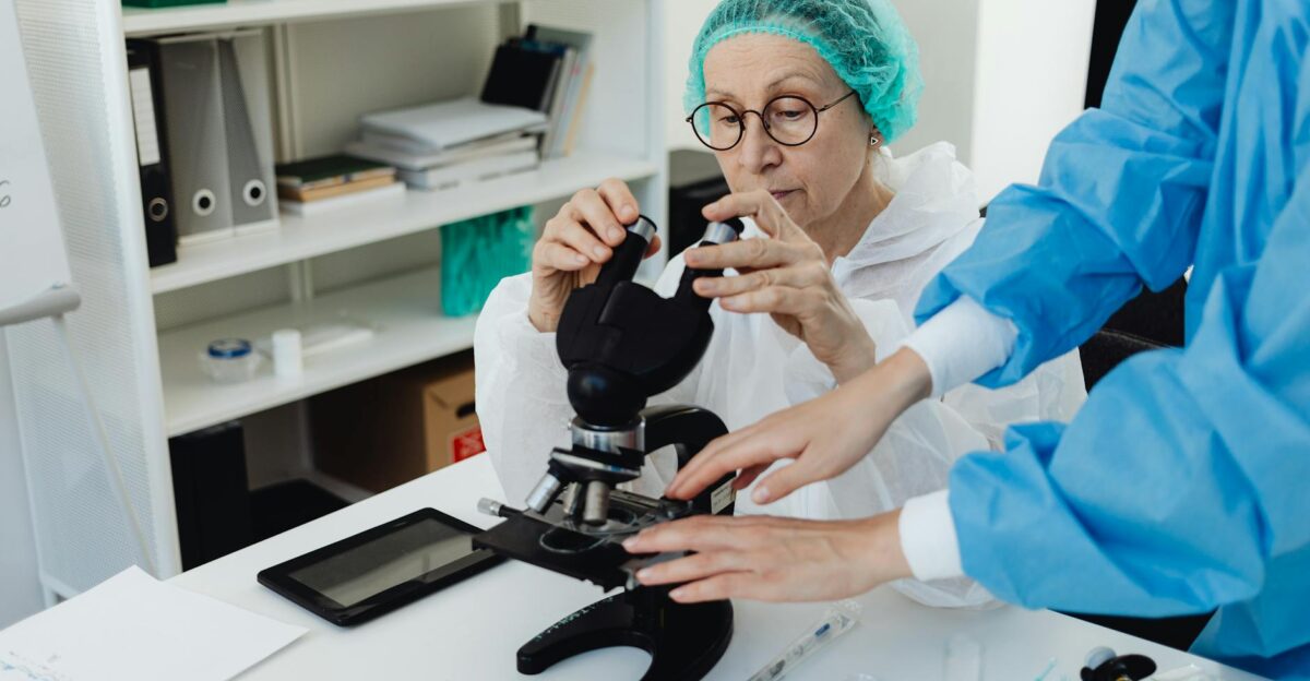 Senior researcher working with a microscope in a laboratory setting assisted by a colleague