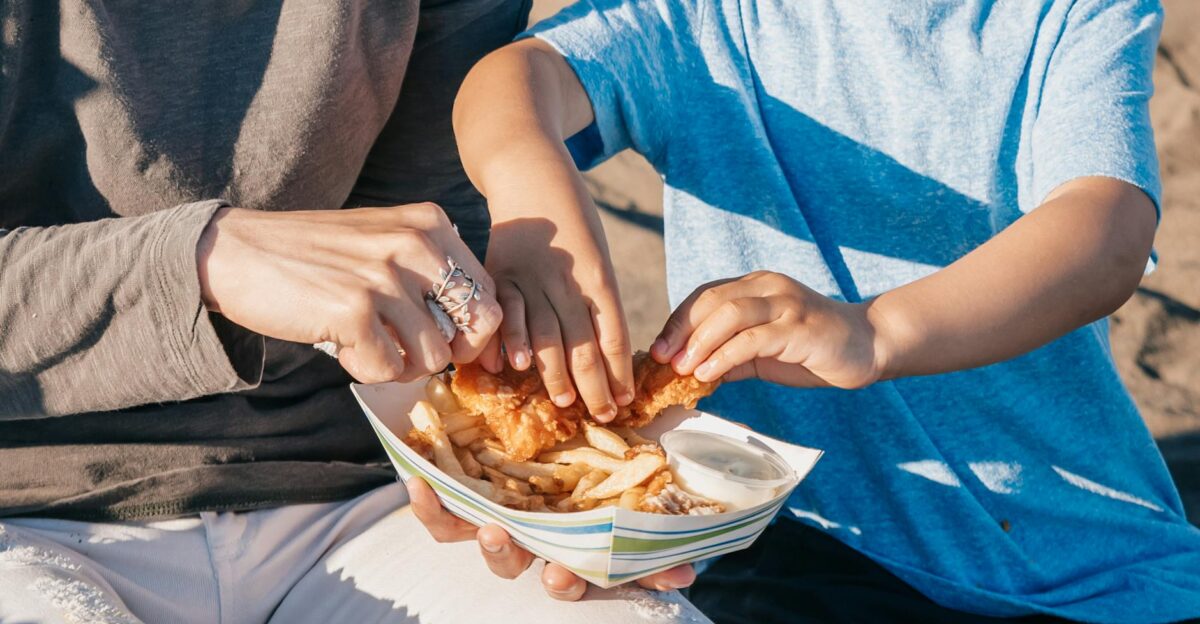 A parent and child sharing a meal of french fries outdoors enjoying togetherness
