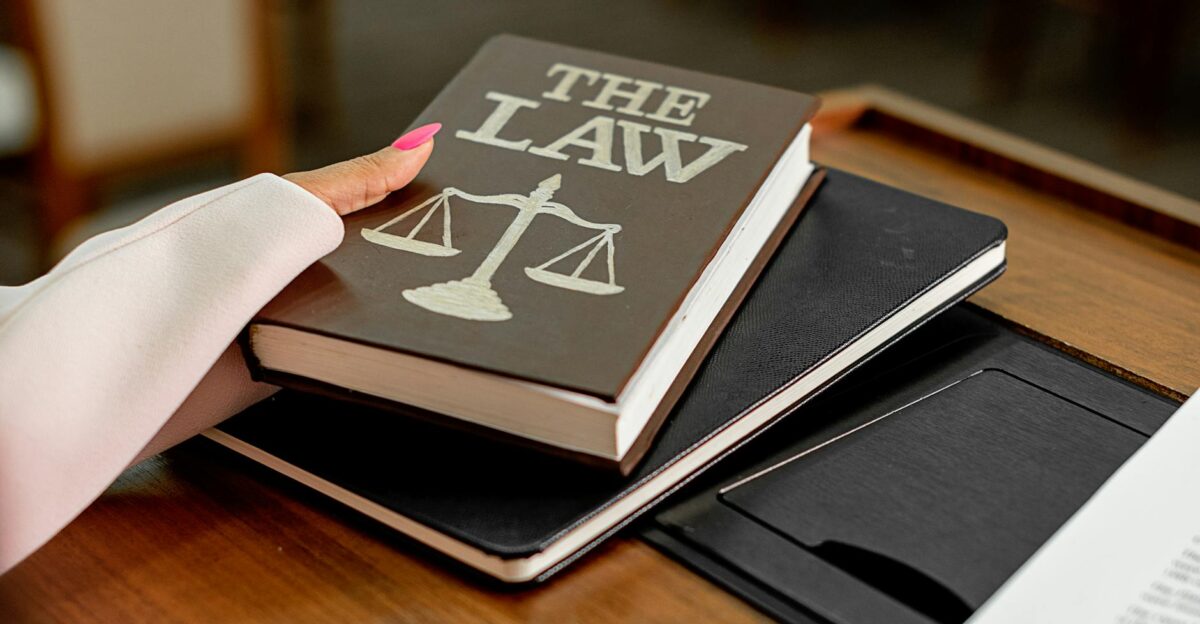 Closeup image of a law book titled The Law on a wooden desk with scales of justice
