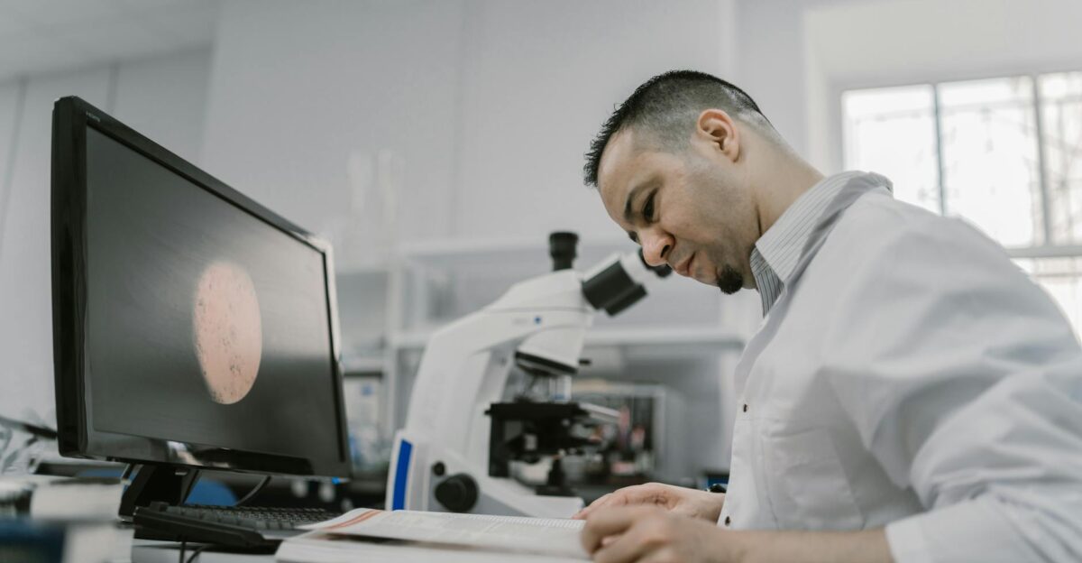 Asian man reading in a laboratory surrounded by equipment and microscope focused on work