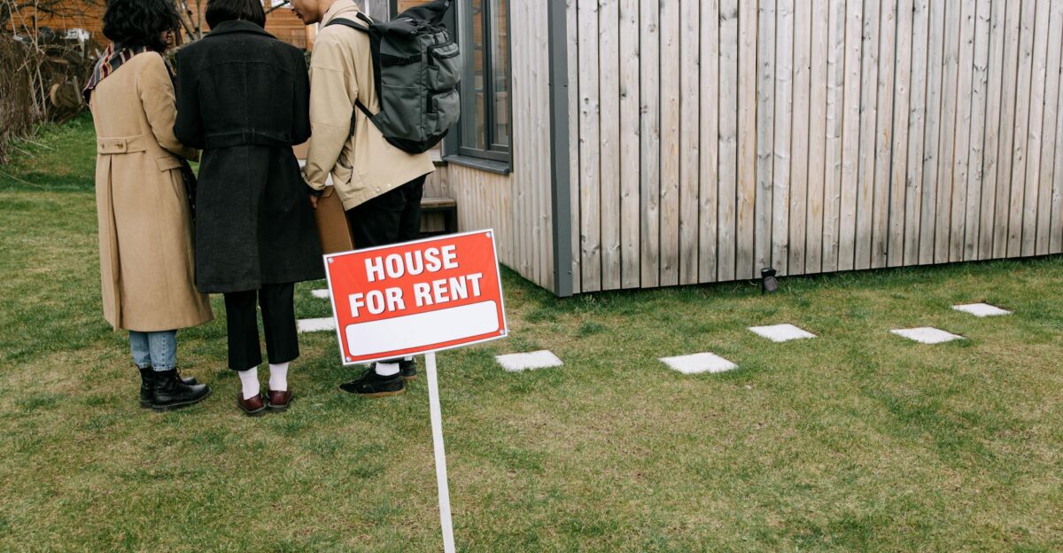 Group of adults viewing a wooden house with a House for Rent sign on the lawn