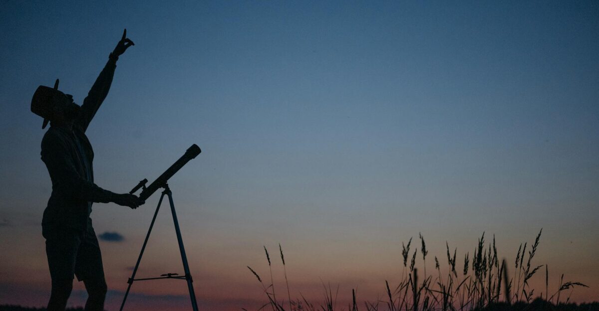 Silhouette of a person pointing at the sky with a telescope during twilight