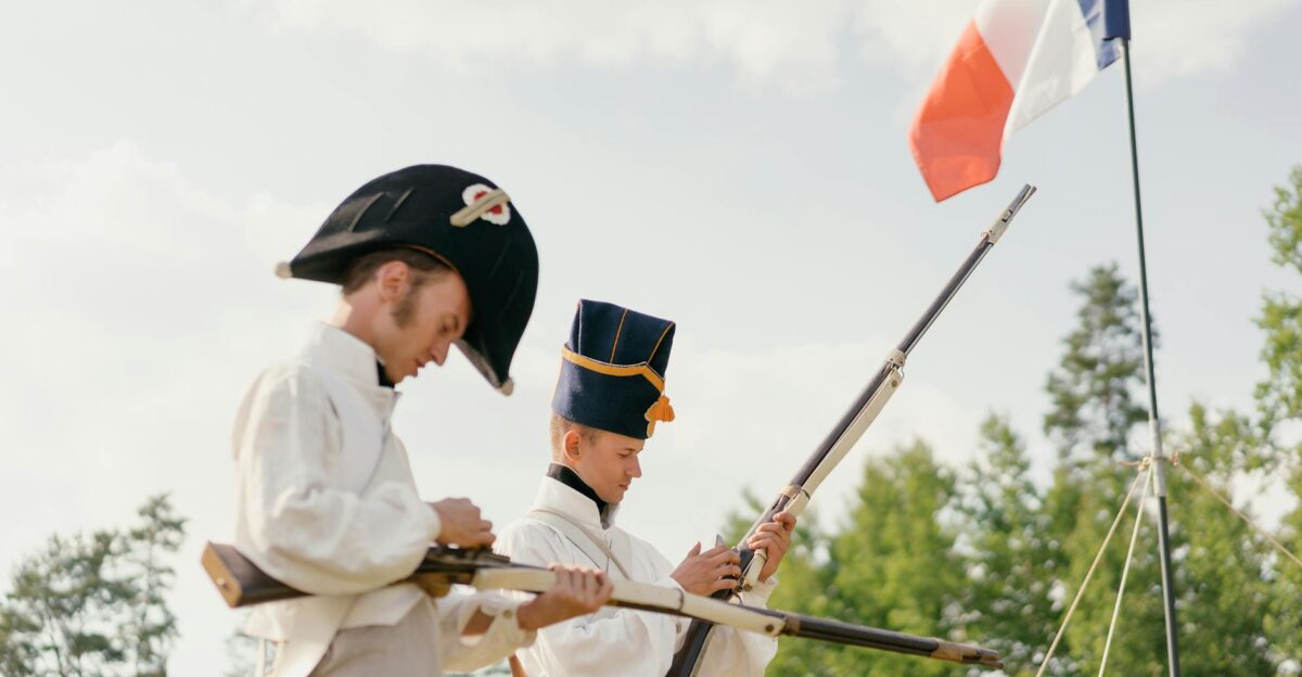 Two reenactors dressed as French soldiers in a historical setting with a flag
