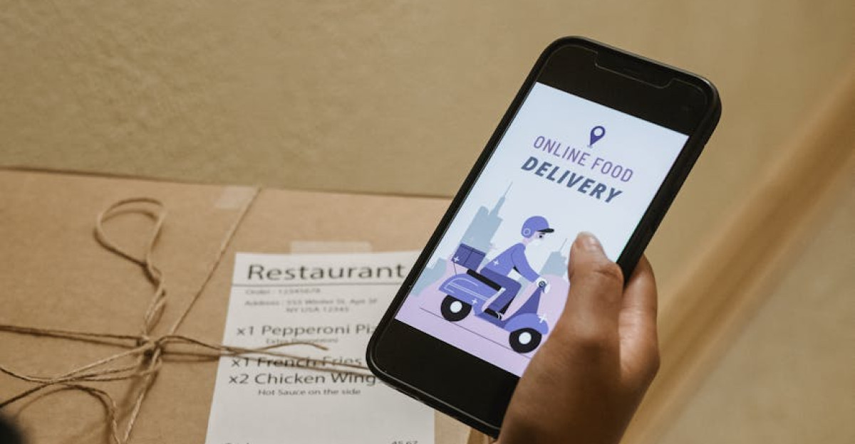 A person holding a phone displaying an online food delivery app next to a pizza box indoors