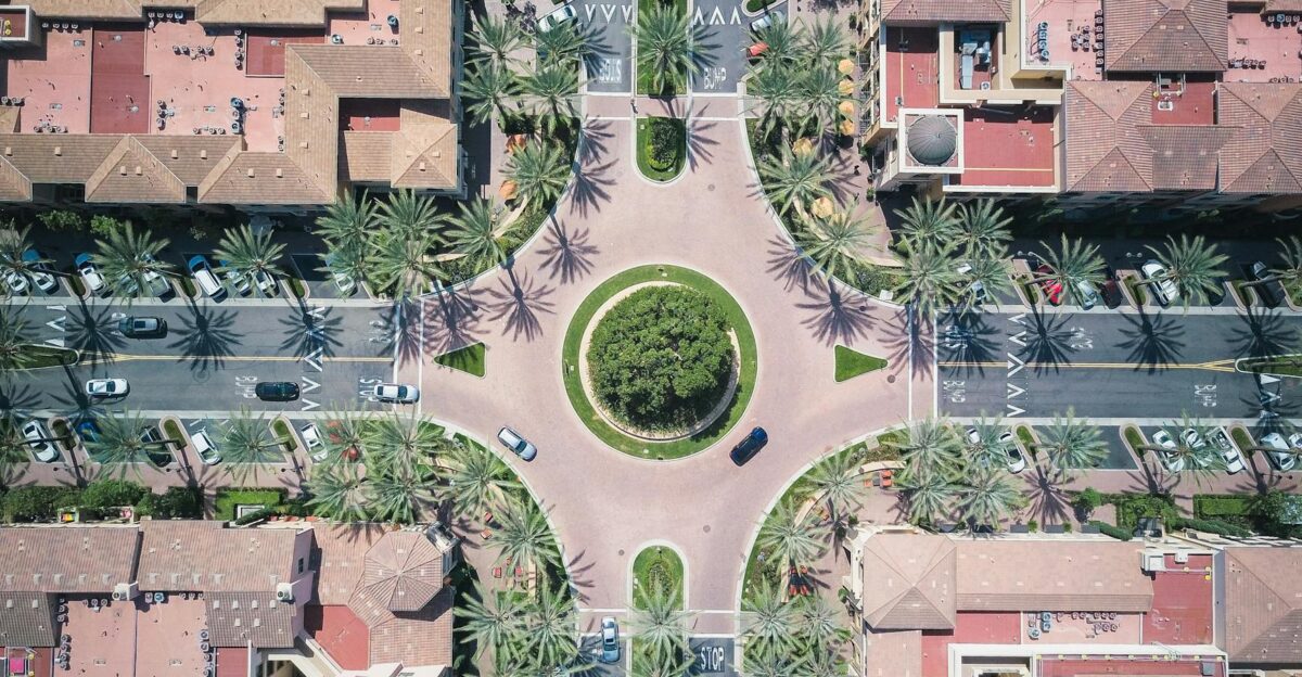 Aerial view of a vibrant cityscape featuring a roundabout with palm trees and urban infrastructure