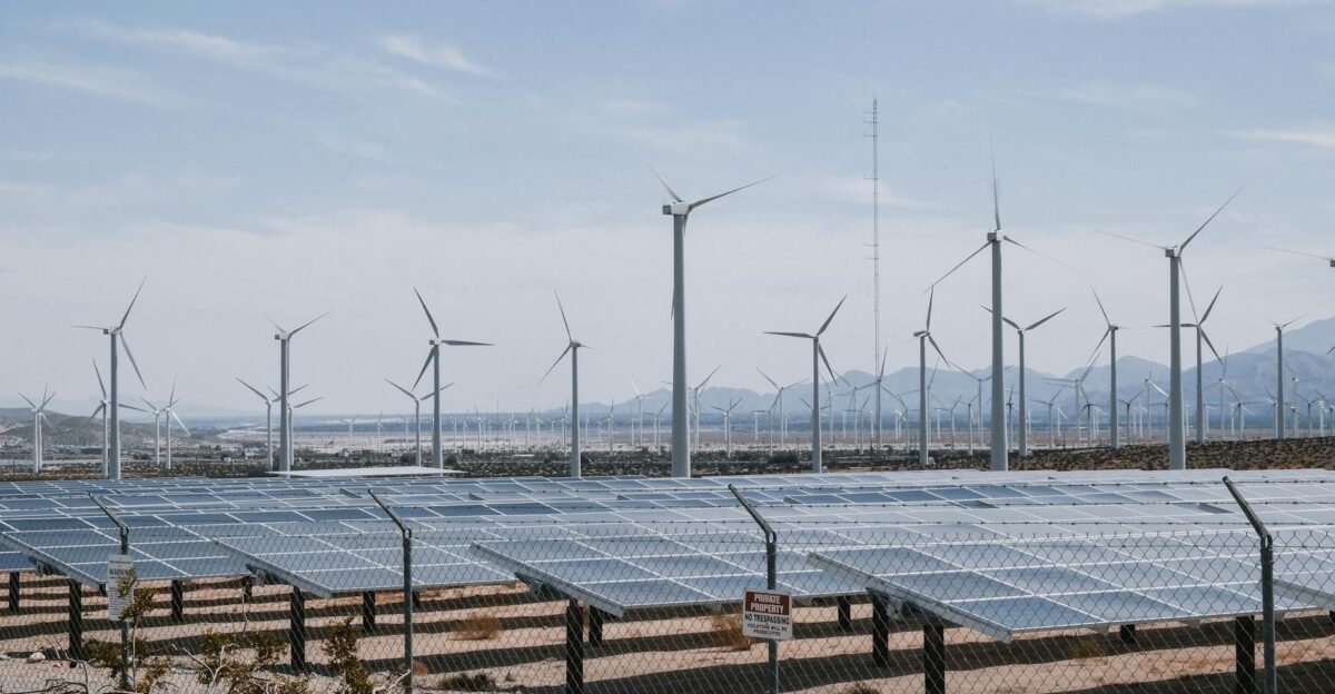 A renewable energy farm with wind turbines and solar panels under a clear sky