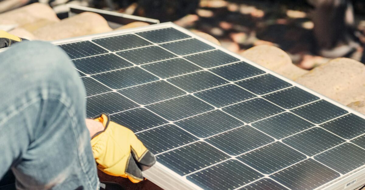A worker installs a solar panel on a sunlit rooftop exemplifying renewable energy