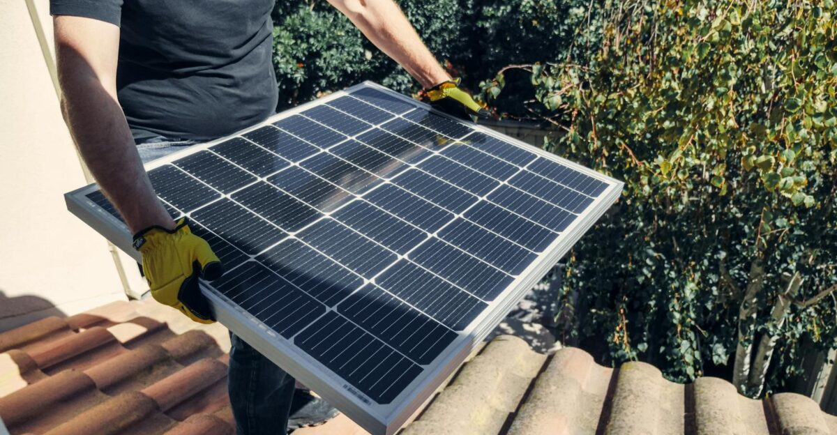 A worker installs a solar panel on a rooftop amidst lush greenery