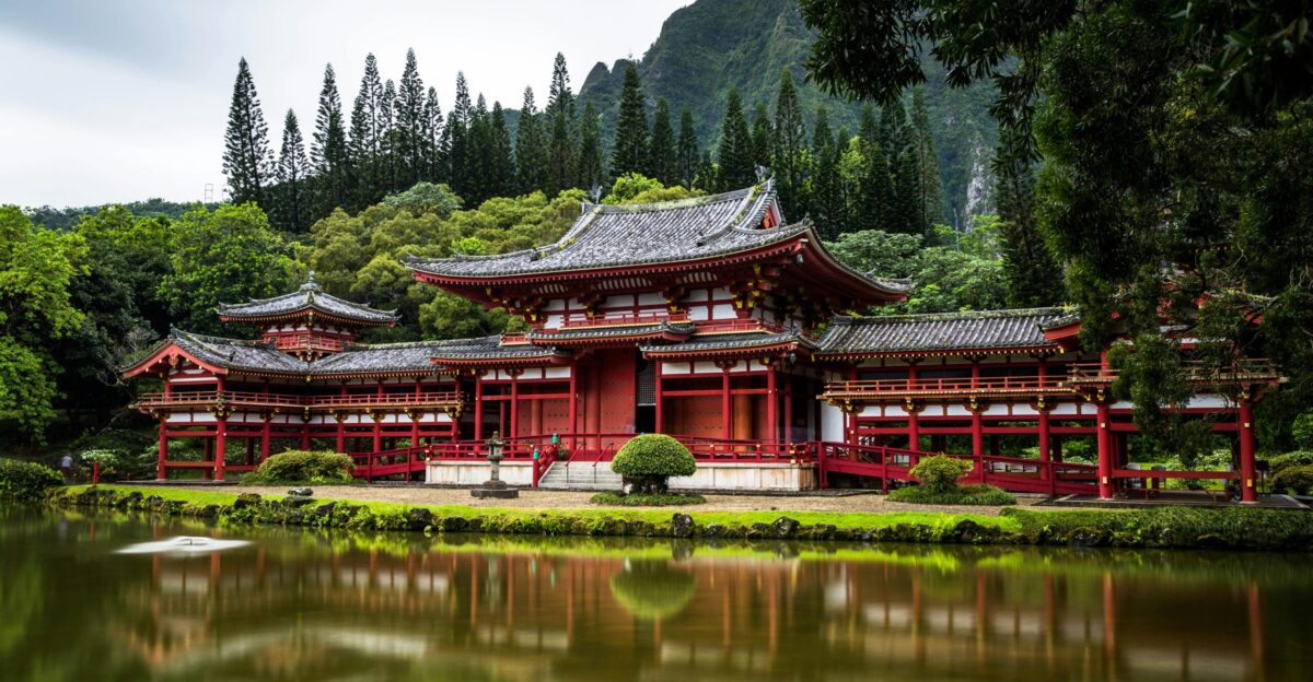 Japanese style temple near calm water behind mountain at daytime