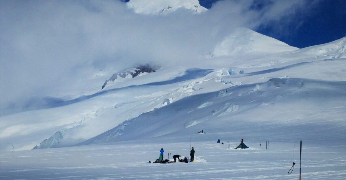 group of people standing on snow near tipi tent and snow covered mountain under white clouds during daytime