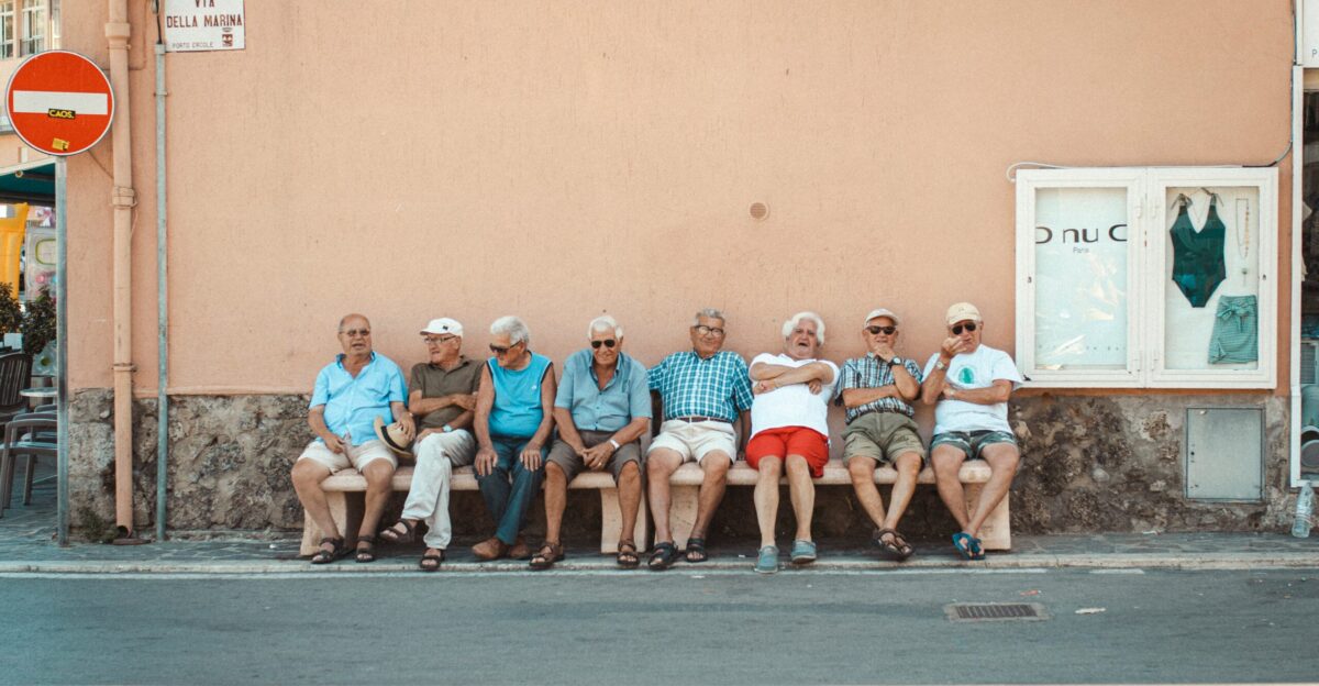 eight men sitting on bench near orange wall during daytime