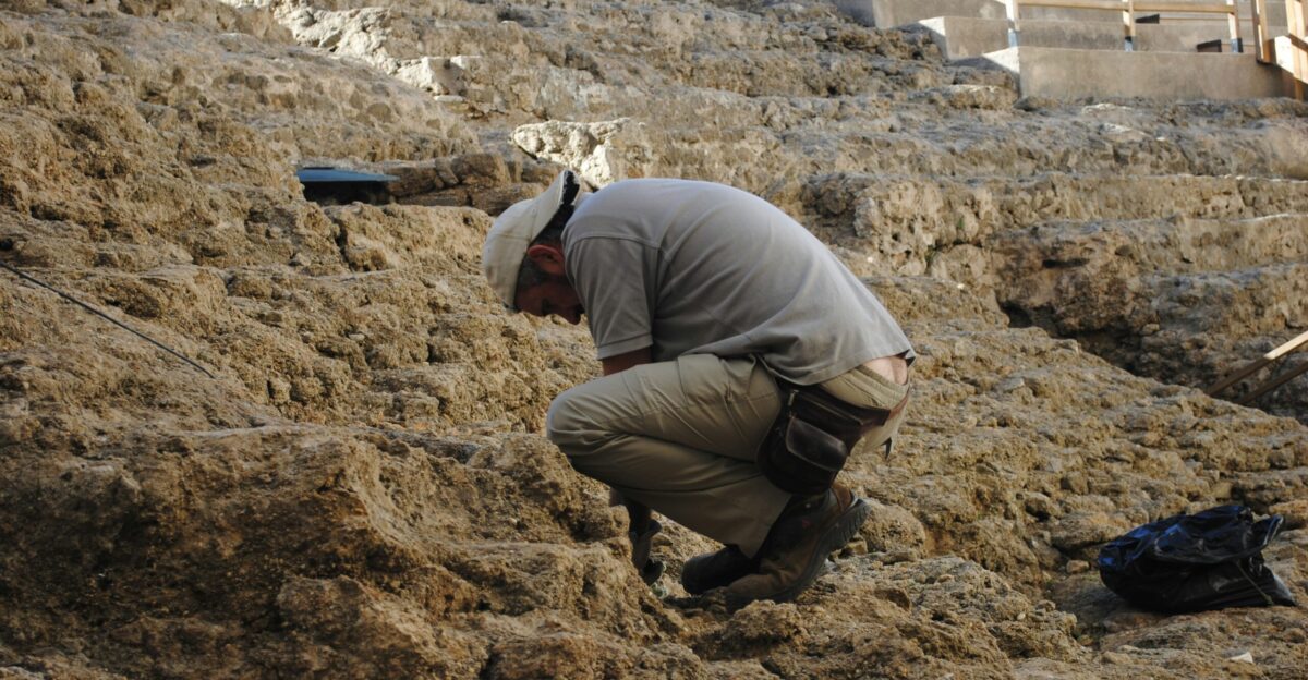 man in gray jacket and brown pants sitting on brown rock during daytime