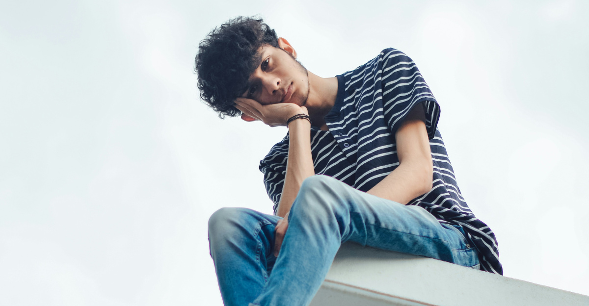 man in blue denim jeans and white and black striped shirt sitting on white concrete wall