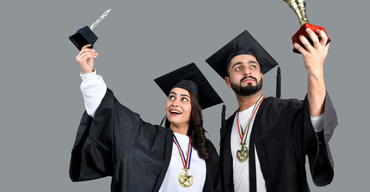 a man and woman wearing graduation gowns and holding a trophy