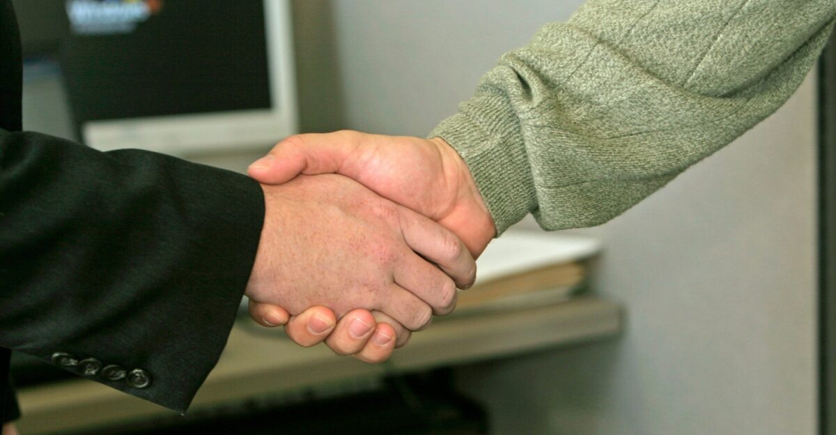 two people shaking hands in front of a computer monitor