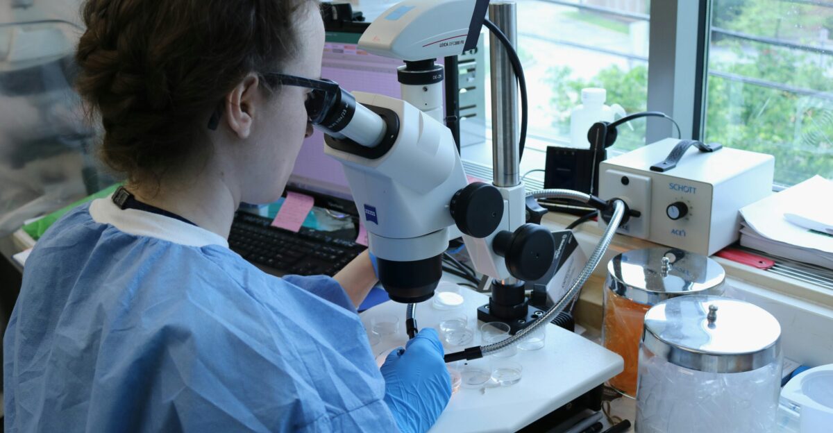 a woman in a lab coat looking through a microscope
