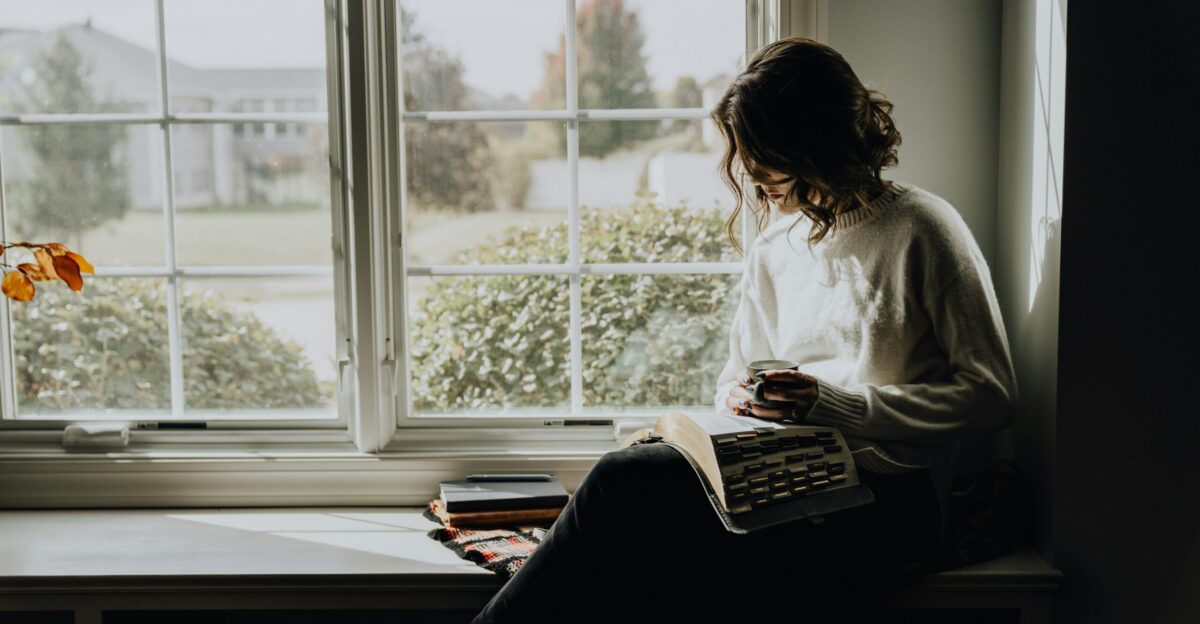 A woman sitting on a window sill reading a book