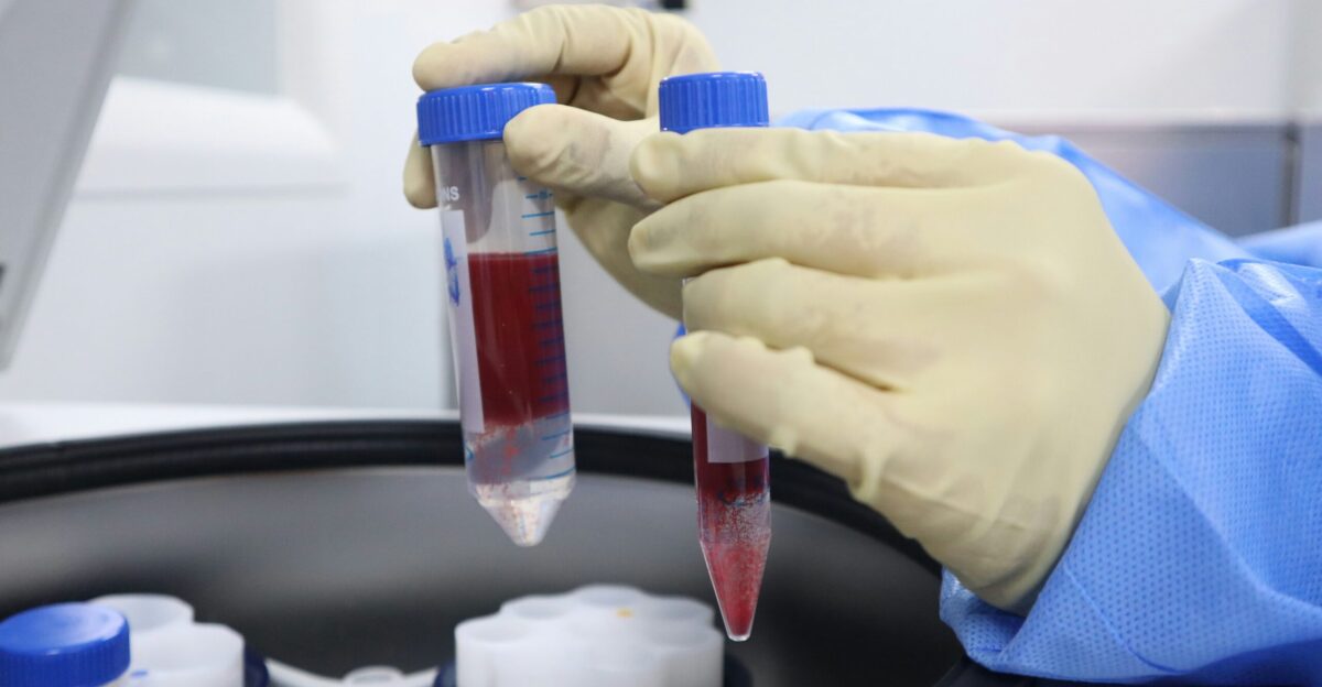 A gloved hand holding a tube of blood